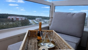 Una bandeja de mimbre con una botella de champán, dos copas y una bandeja en un balcón con vistas a edificios y árboles.