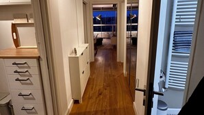 Un pasillo con piso de madera, armarios blancos y vistas a un balcón con cielo nocturno.