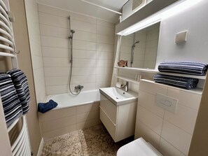 A compact bathroom with a shower, a sink, and a toilet. There are towels and a mirror above the sink. - Vacation apartment in Sahlenburg with sea view (Cuxhaven)