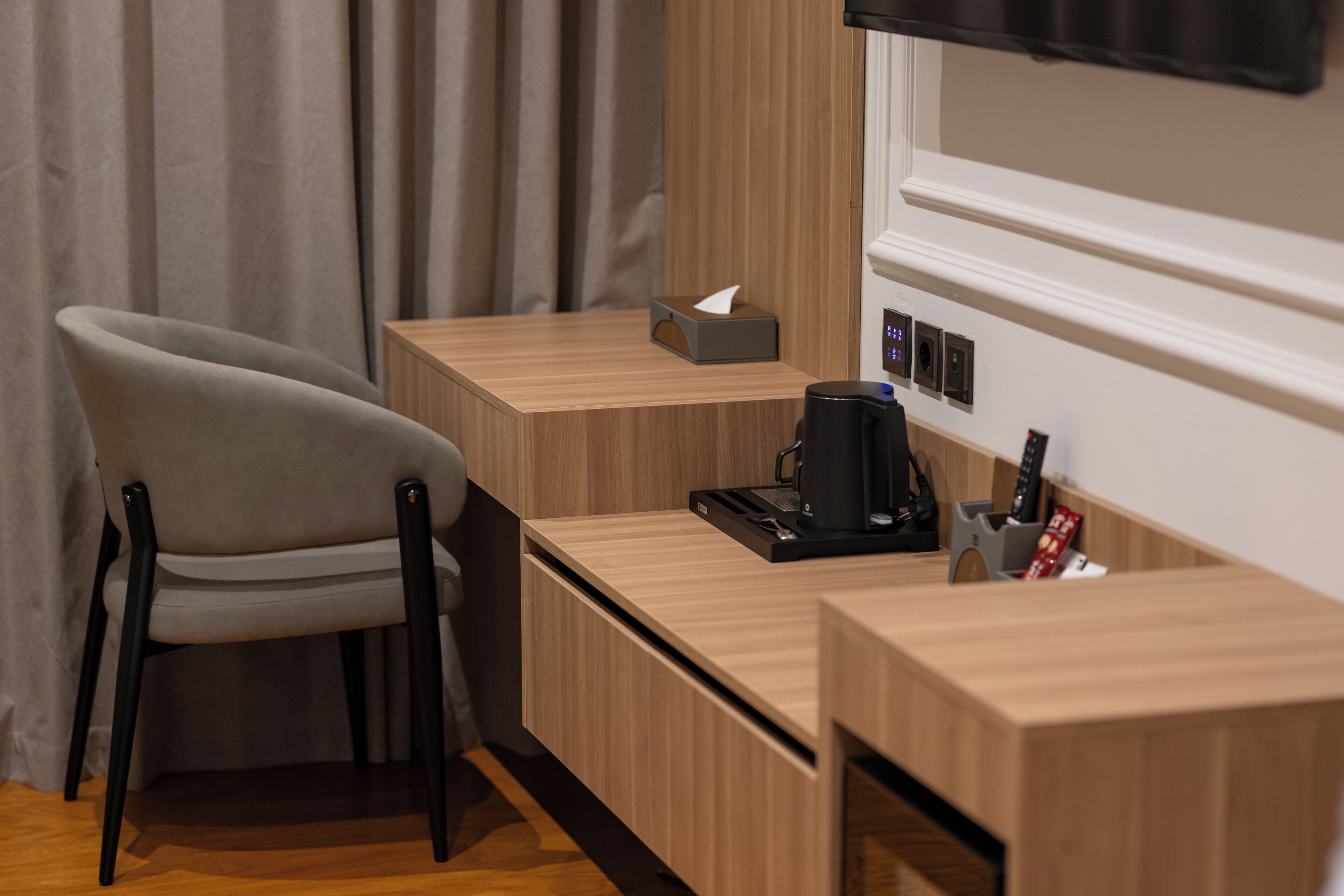 A modern hotel room with a wooden desk, a chair, a coffee machine, and a tissue box.