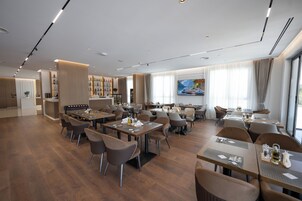 Un restaurante moderno con varias mesas y sillas, un área de bar con botellas y un ventanal con un cuadro.