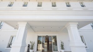 Entrada de hotel con porche cubierto, columnas grandes y plantas en macetas.