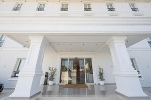 Entrada de hotel con porche cubierto, columnas grandes y plantas en macetas.