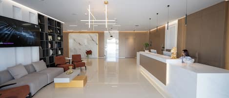 A modern hotel lobby with a reception desk, seating area, and a large flat-screen TV.