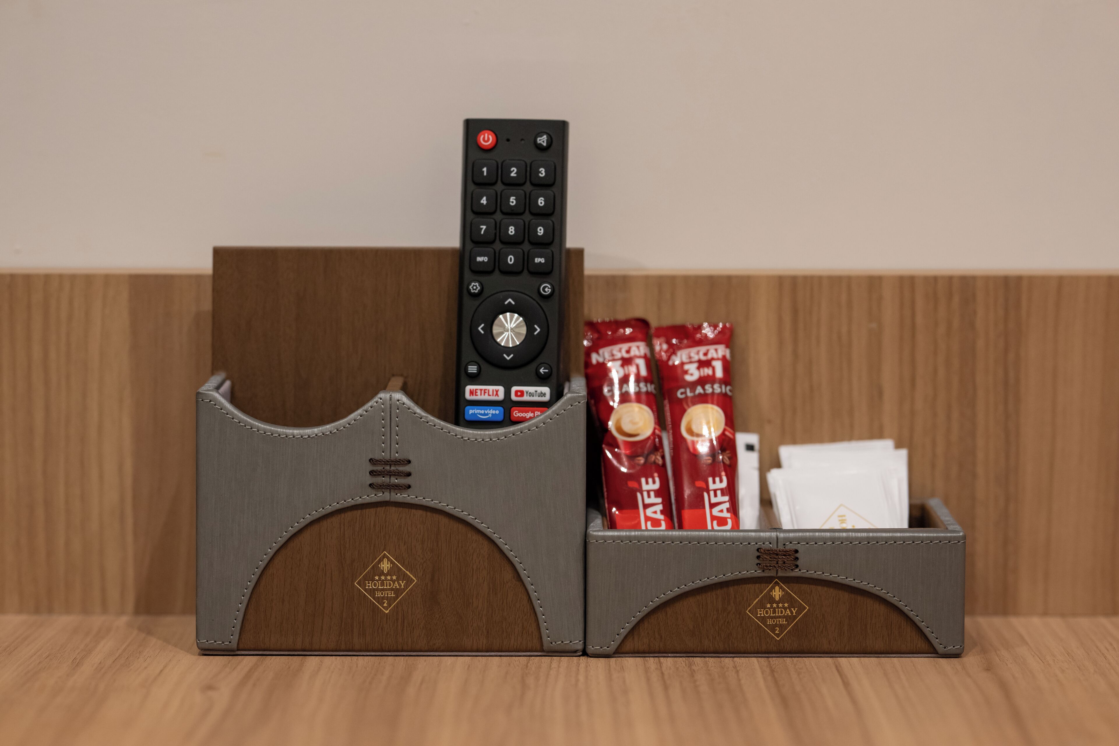 A remote control and two red beverage packs in a leatherette holder with a hotel logo.