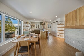 A modern kitchen with wooden flooring, a dining area with a table set for four, and a view of the outdoors through large windows. - Mountain-view Pagosa Springs house on five acres with four bedrooms, three baths, private hot tub, two fireplaces, chef's kitchen, and entertainment room; sleeps 7. (Pagosa Springs)
