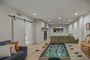 Una sala moderna con mesa de futbolín, sofá, mesa de comedor y chimenea.