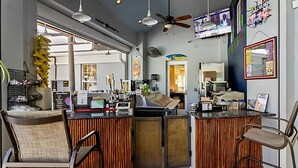 A bar area with a counter, chairs, ceiling fans, and a TV screen.