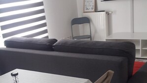 A modern living room with a sofa set, a dining table with a chair, a TV mounted on the wall, and a radiator. - Nice apartmentvery quiet (Bobigny)