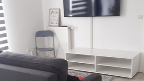A living room with a grey sofa, a white entertainment unit, and a flat-screen TV mounted on the wall. - Nice apartmentvery quiet (Bobigny)