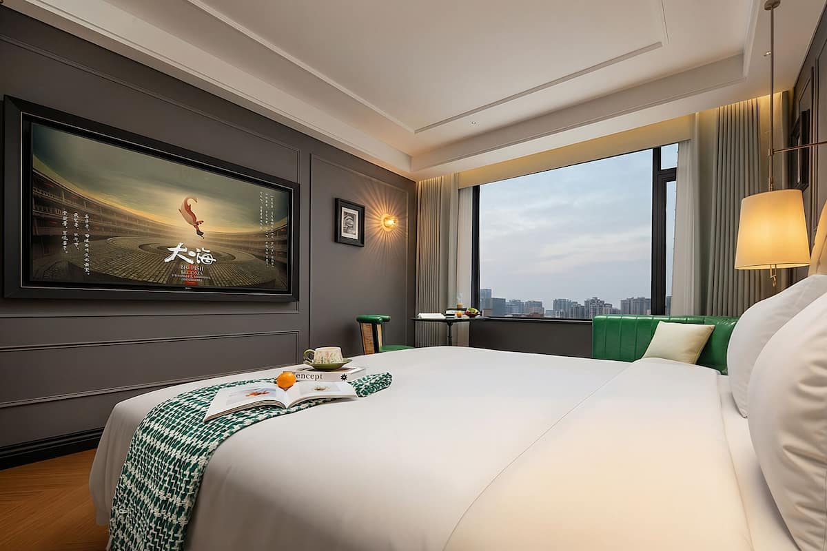 A hotel room with a large bed, a city view, a television, and a window with curtains.