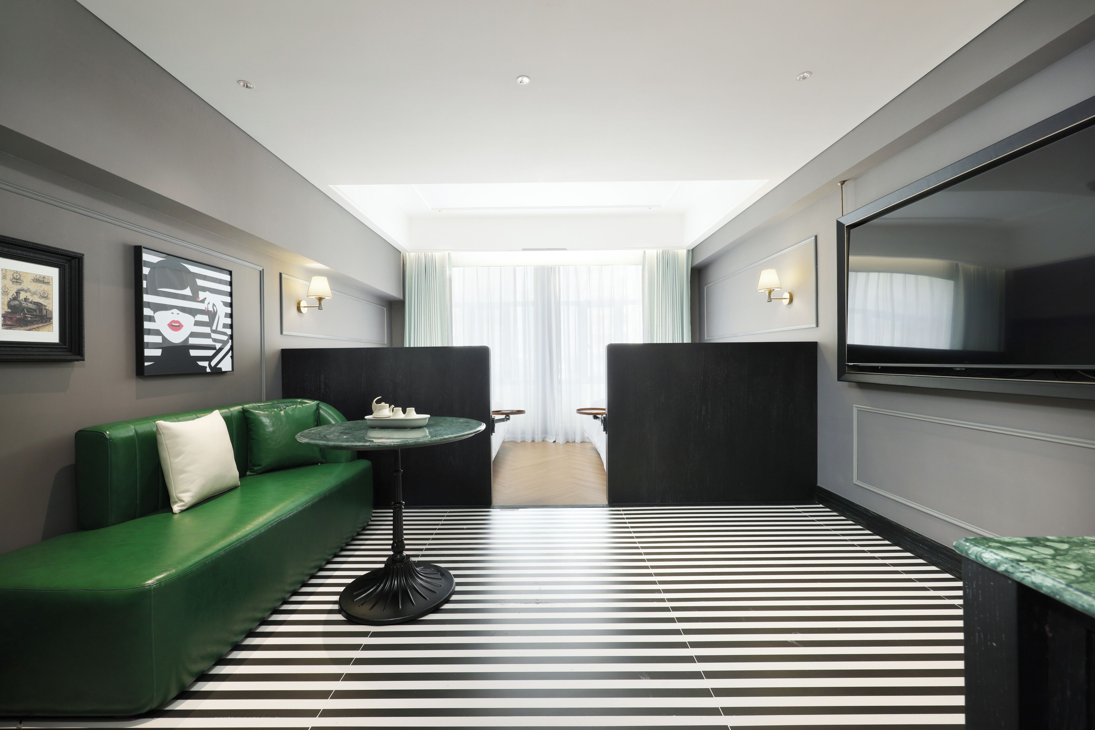A modern hotel room with a green sofa, a round table, and a large TV.