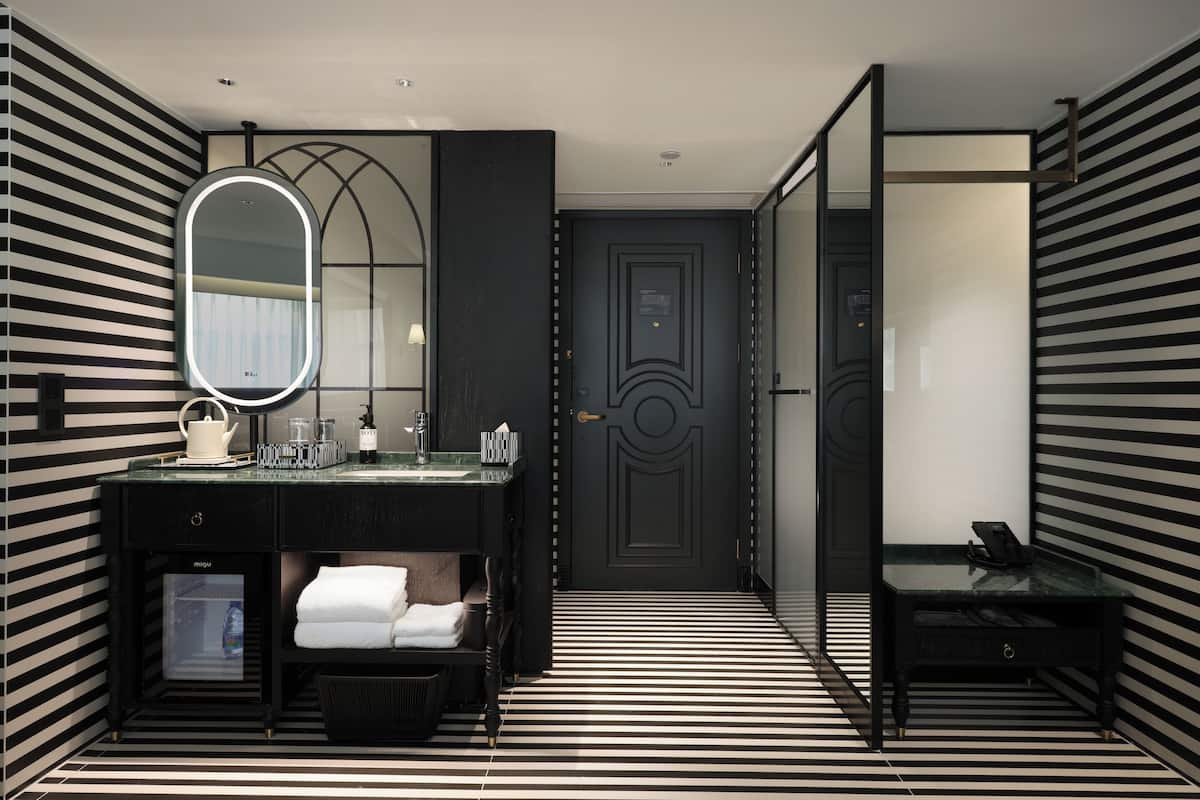 A modern bathroom with a black and white striped floor, a large mirror, a sink with a glass top, and a dark door.