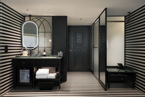 Une salle de bain moderne avec un sol à rayures noires et blanches, un grand miroir, un lavabo avec un plateau en verre et une porte sombre.