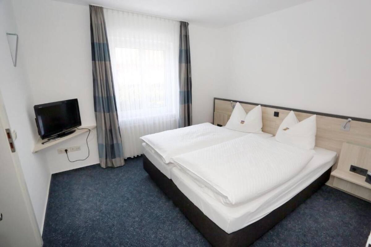 Une chambre d’hôtel avec un lit, un téléviseur posé sur un meuble et une fenêtre avec des rideaux.