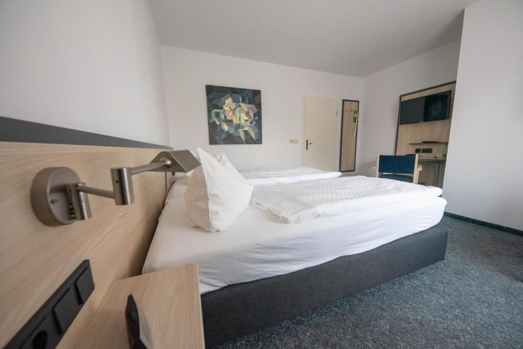 A hotel room with a bed, a bedside table, a wall-mounted TV, and a painting on the wall.