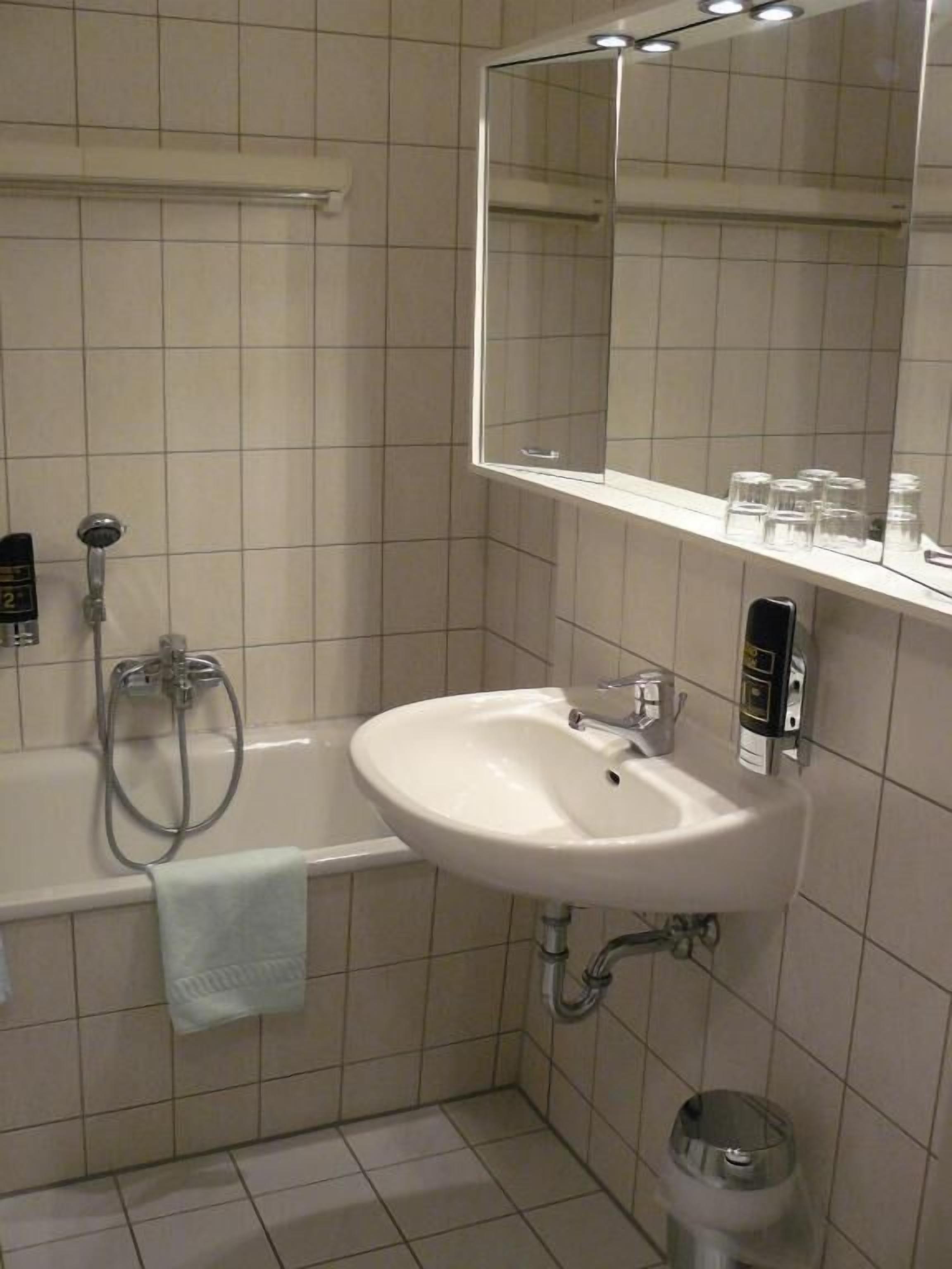 Ein modernes Badezimmer mit einem weißen Waschbecken, einer Duschbrause, einem Handtuchhalter und einem Spiegel.