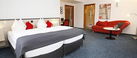 Una habitación de hotel con una cama grande, un sofá rojo, una mesita pequeña y un escritorio con una silla.