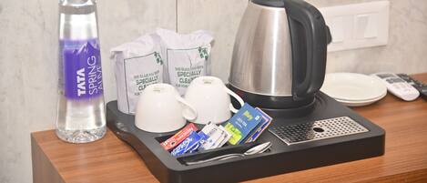 A hotel room's breakfast tray with a TATA SPRING water bottle, two white coffee cups, a black electric kettle, a tray with tea bags, a remote control, and a spoon.