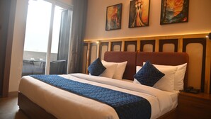 A hotel room with a large bed, a desk, and a chair. There are three paintings on the wall. - AARUSH HOTEL & RESORT (Lalkuwa)