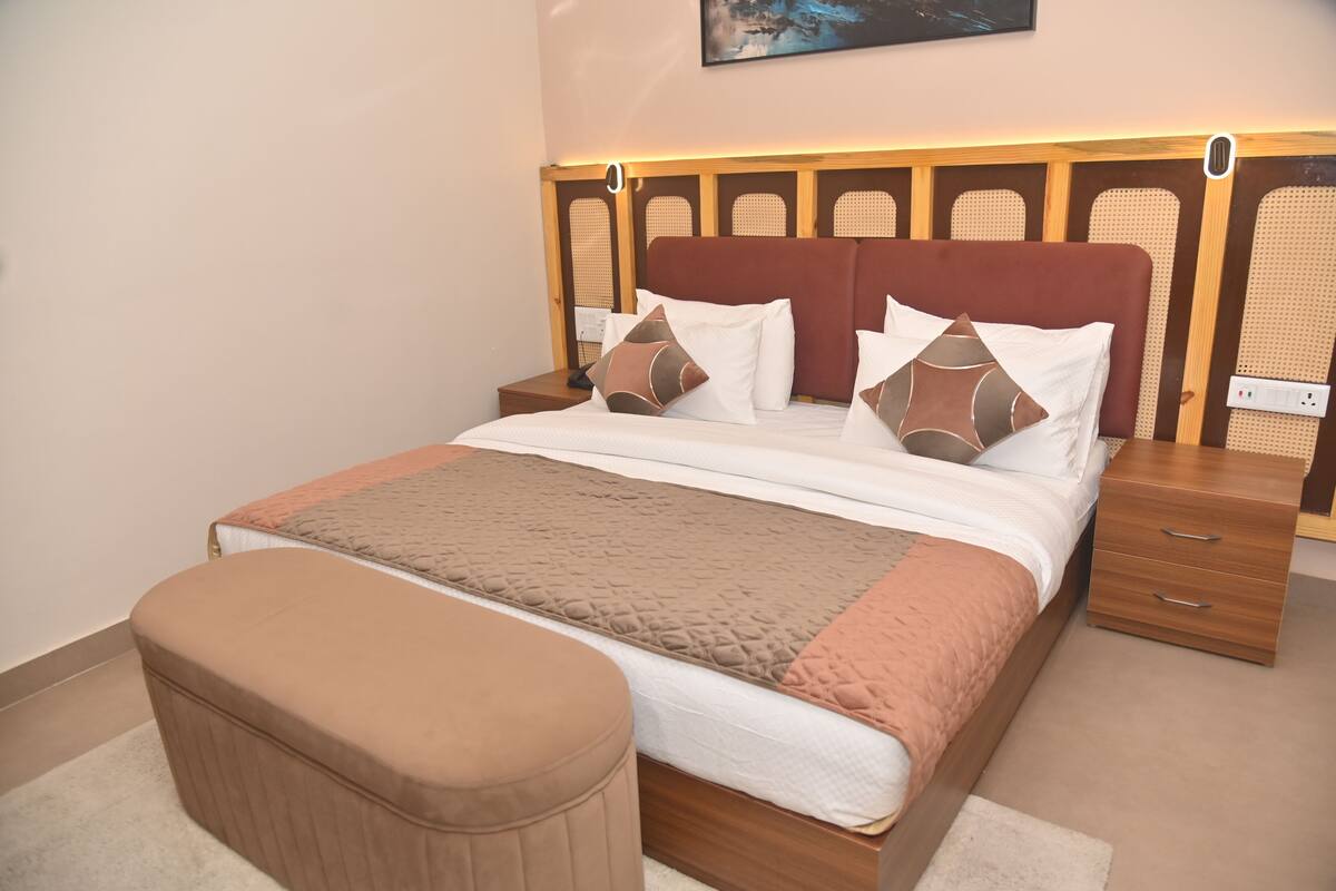 A neatly made bed with a wooden headboard, a bedside table, and a matching ottoman.
