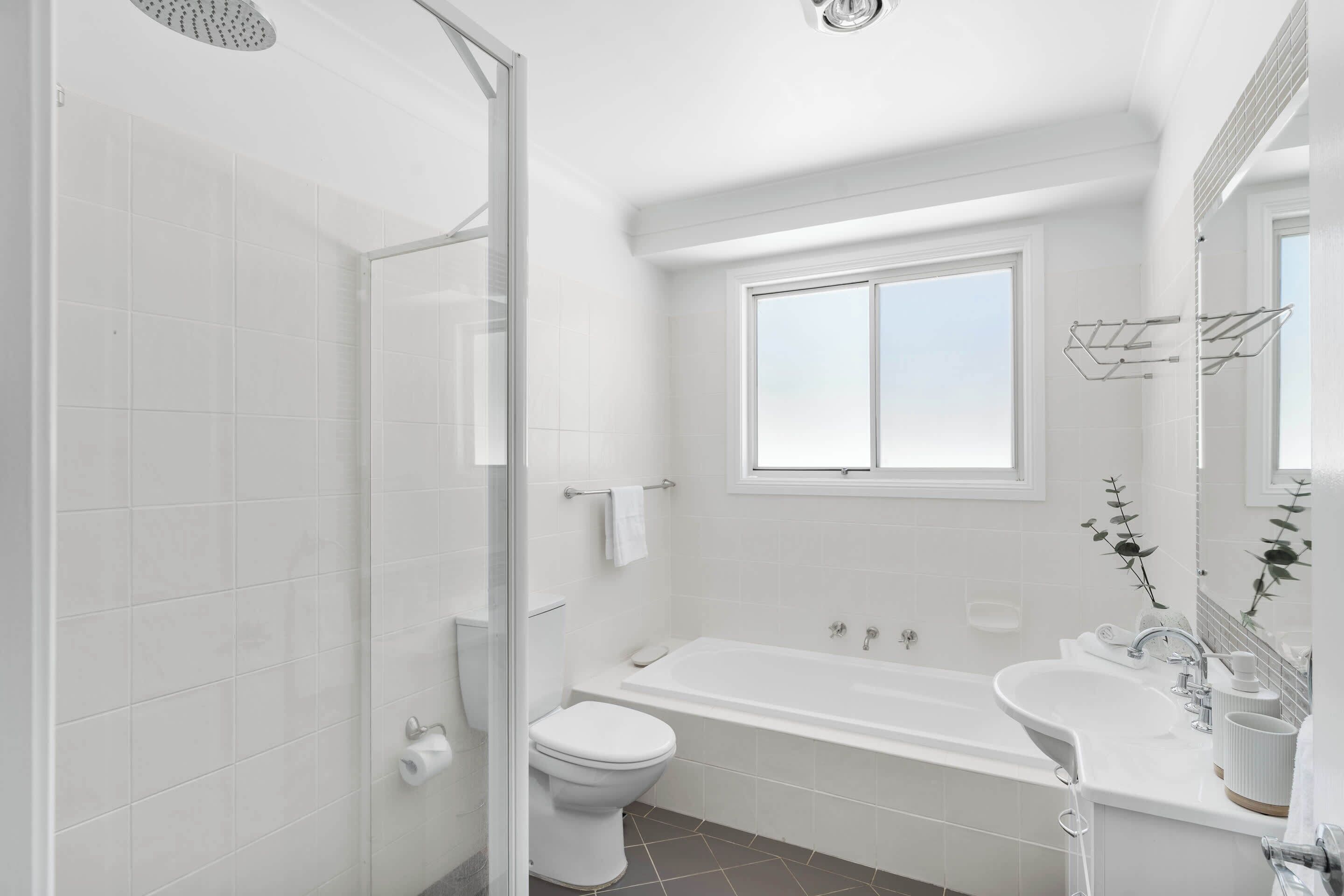 A modern bathroom with a glass shower enclosure, a toilet, a bathtub, and a sink.
