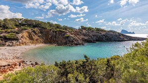 A coastal landscape with a rocky beach, clear turquoise waters, and a mountainous backdrop. - Villa 'Casa Arola' with Sea Views, Wi-Fi and Air Conditioning (Sant Josep de sa Talaia)