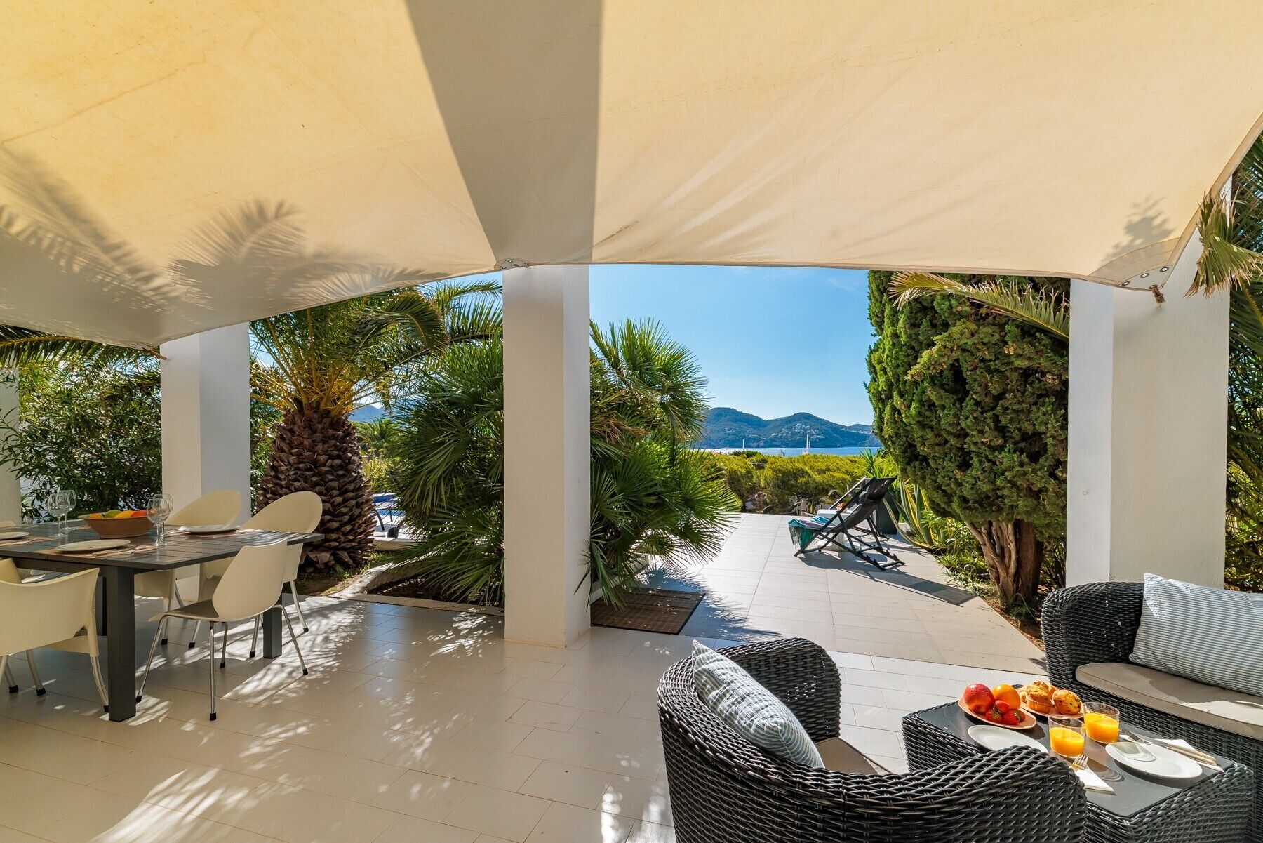 An outdoor patio with a table set for two, wicker furniture, and a view of the sea and hills. - Villa 'Casa Arola' with Sea Views, Wi-Fi and Air Conditioning (Sant Josep de sa Talaia)