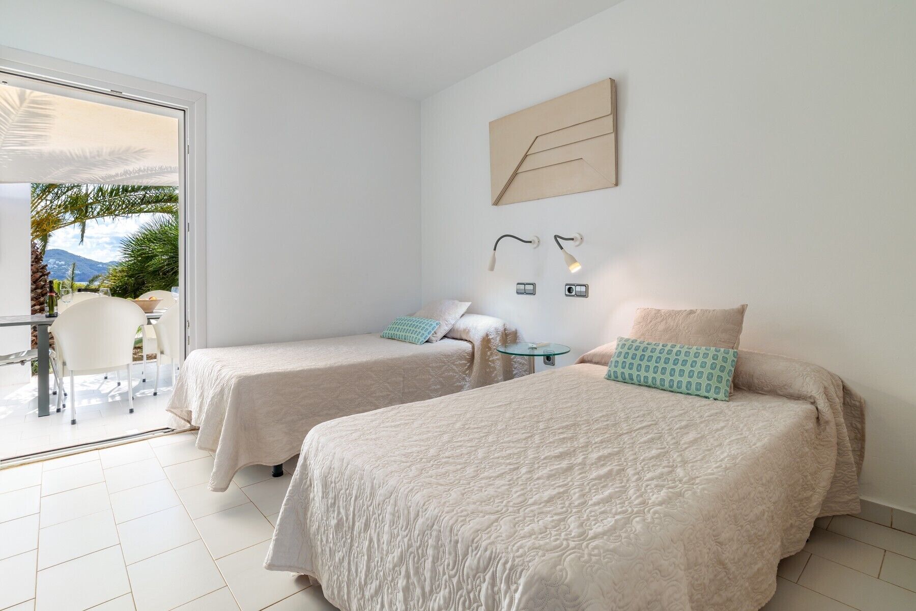 Habitació d'hotel amb dos llits, una taula petita i un balcó amb vista.