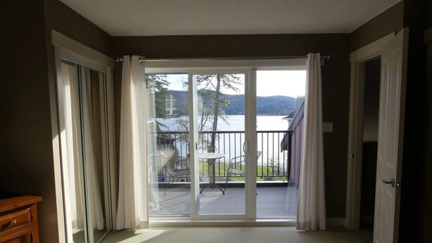 Een hotelkamer met een grote schuifglazen deur die leidt naar een balkon met uitzicht op een meer en bergen.