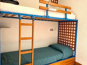 Un lit superposé avec une échelle en bois, une petite étagère et un luminaire fixé au mur.