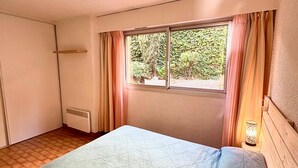 Une petite pièce simple, avec un lit, une fenêtre avec des rideaux, un radiateur et une lampe.