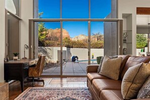 A modern living room with a large sliding glass door, a leather sofa, a desk, and a patterned rug. - Peaceful Sedona Retreat, Views, Pool, Hot Tub! (Sedona)