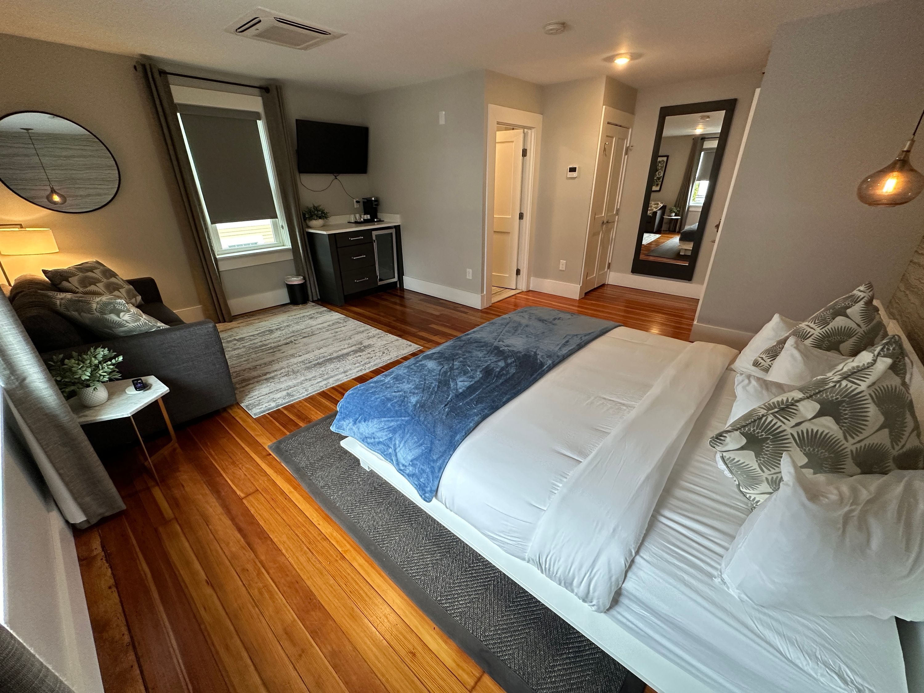 A modern bedroom with a large bed, a desk, a TV, and a mirror.