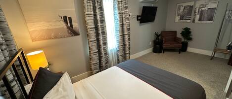 A hotel room with a large bed, a desk with a lamp, a TV, and a window with curtains.
