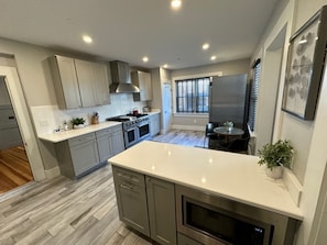 A modern kitchen with grey cabinets, a stainless steel range, and a large island. - Entire Modern 7 Unit 7 Bath Boutique Inn (Newport)