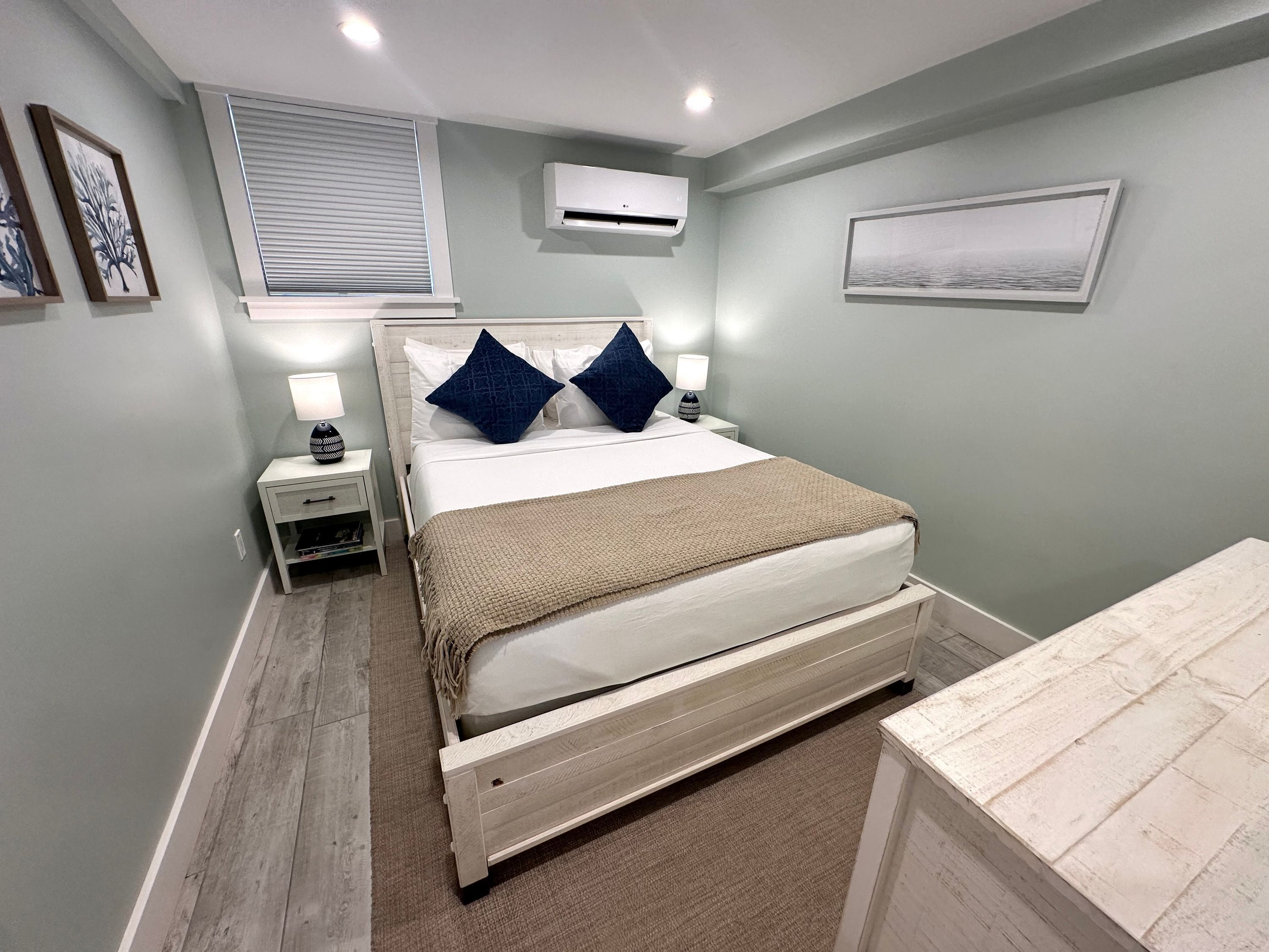A bedroom with a bed, nightstands, an air conditioner, and a window with blinds.