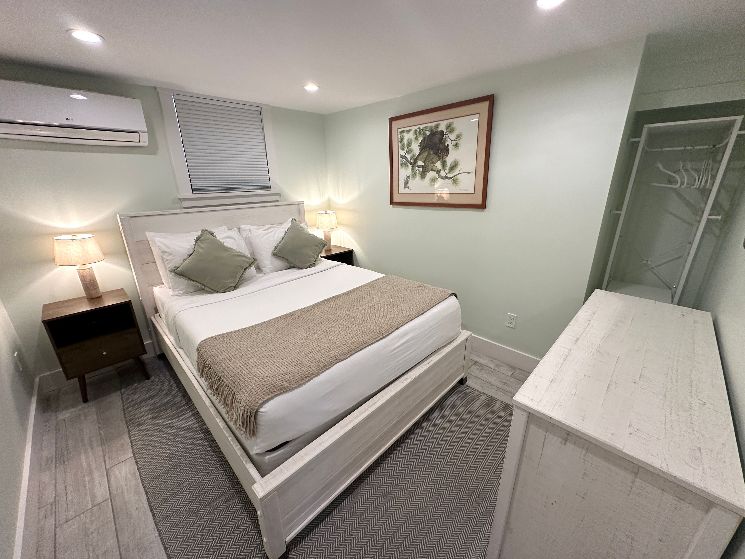 Une chambre à coucher comprenant un lit, des lampes de chevet, un climatiseur fixé au mur, un tableau encadré et une armoire.