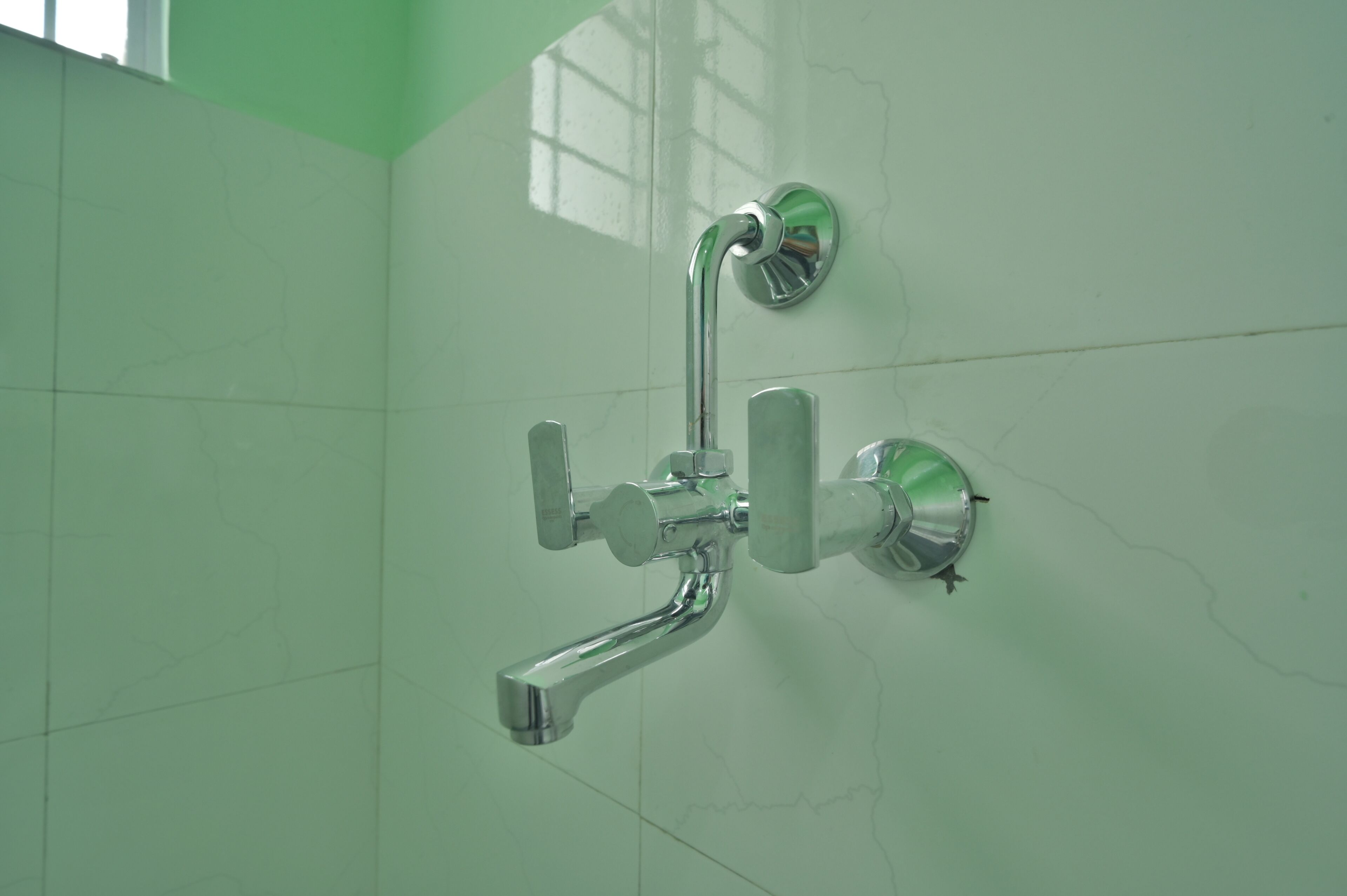 A bathroom with a chrome faucet and shower head, tiled walls, and a visible crack.