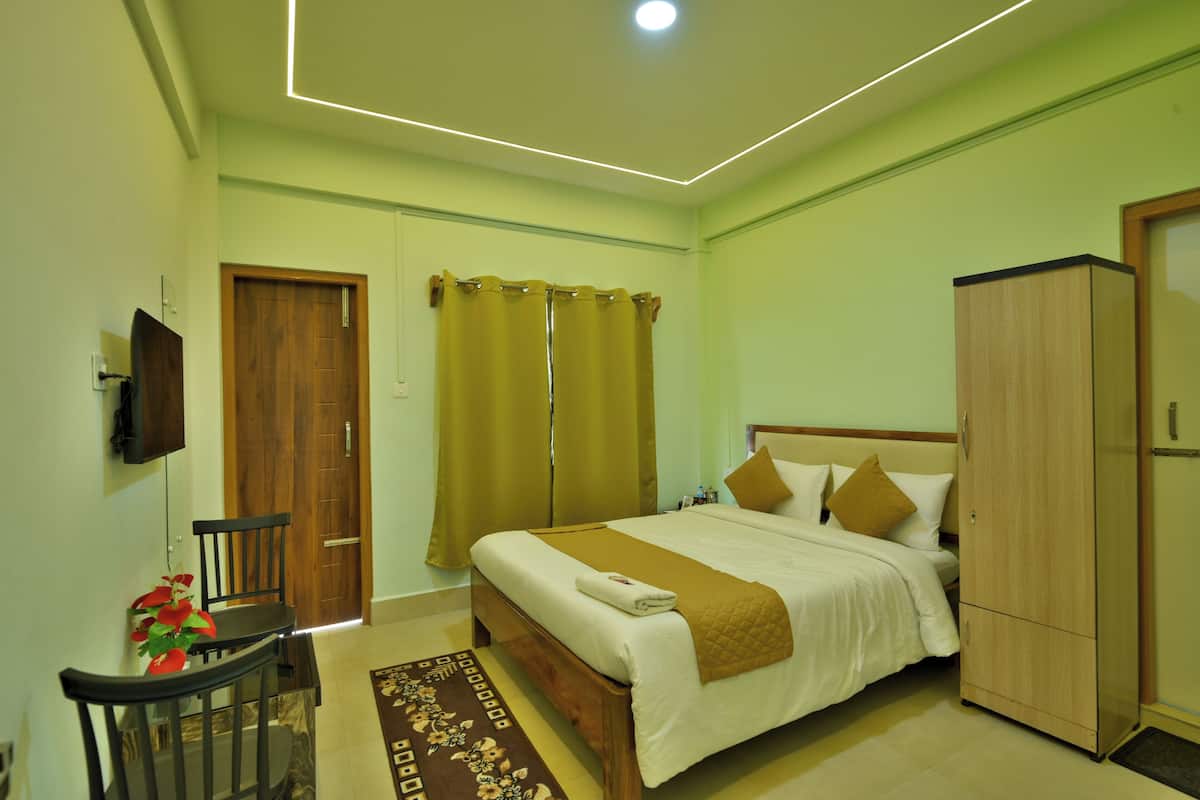 A bedroom with a bed, a wardrobe, a desk with a chair, and a television on the wall.