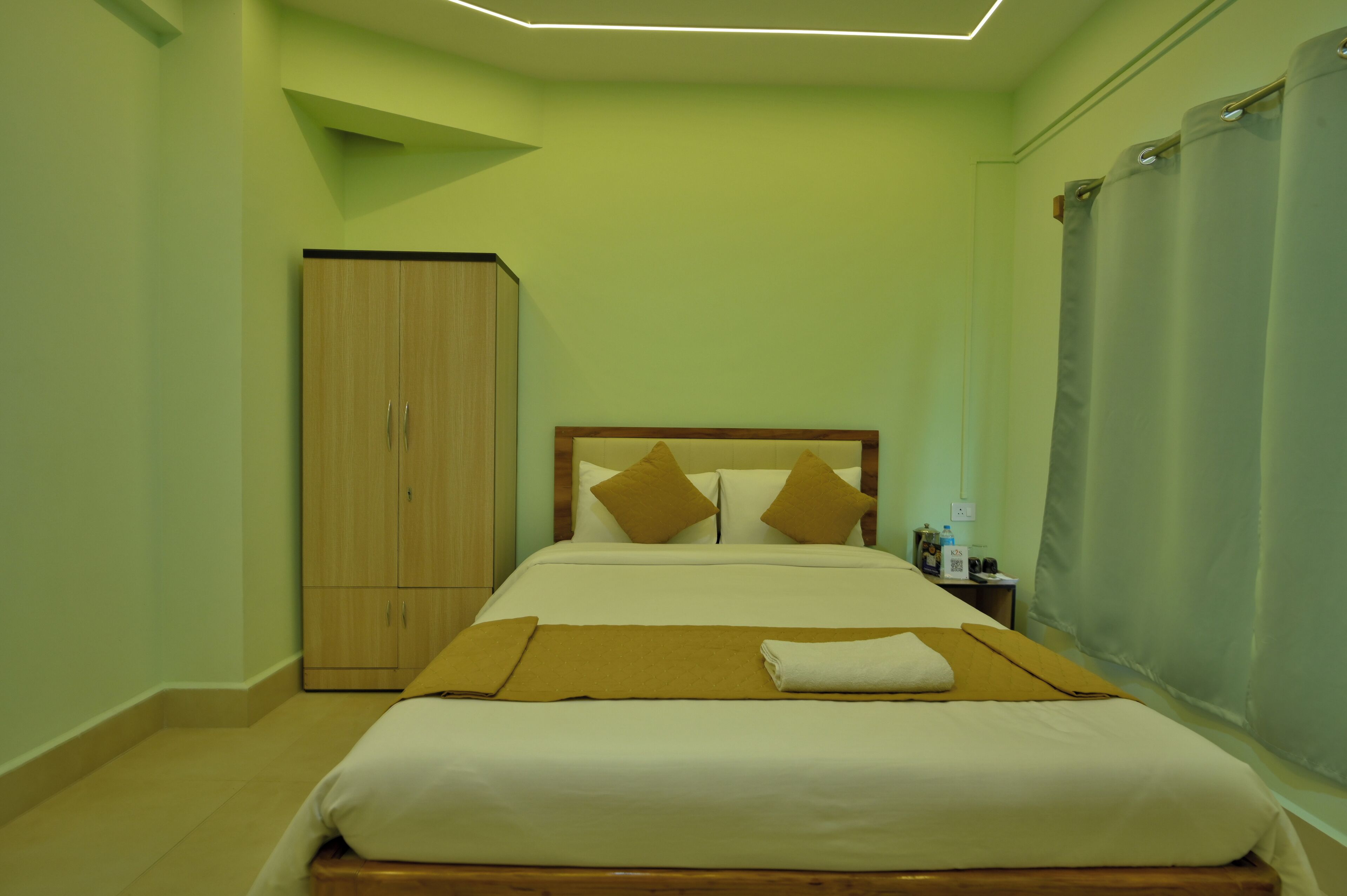 Una cama individual con cabecera de madera, un armario y una mesita de noche con lámpara y botella.