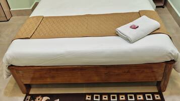 A neatly made bed with a brown quilt and white linens, a wooden headboard, and a floral-patterned rug on the floor.