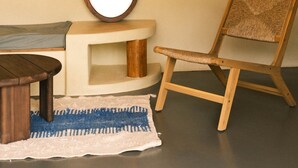 Una stanza con una lampada a soffitto intrecciata, uno specchio rotondo, una sedia di legno, un tavolino e una consolle bianca.