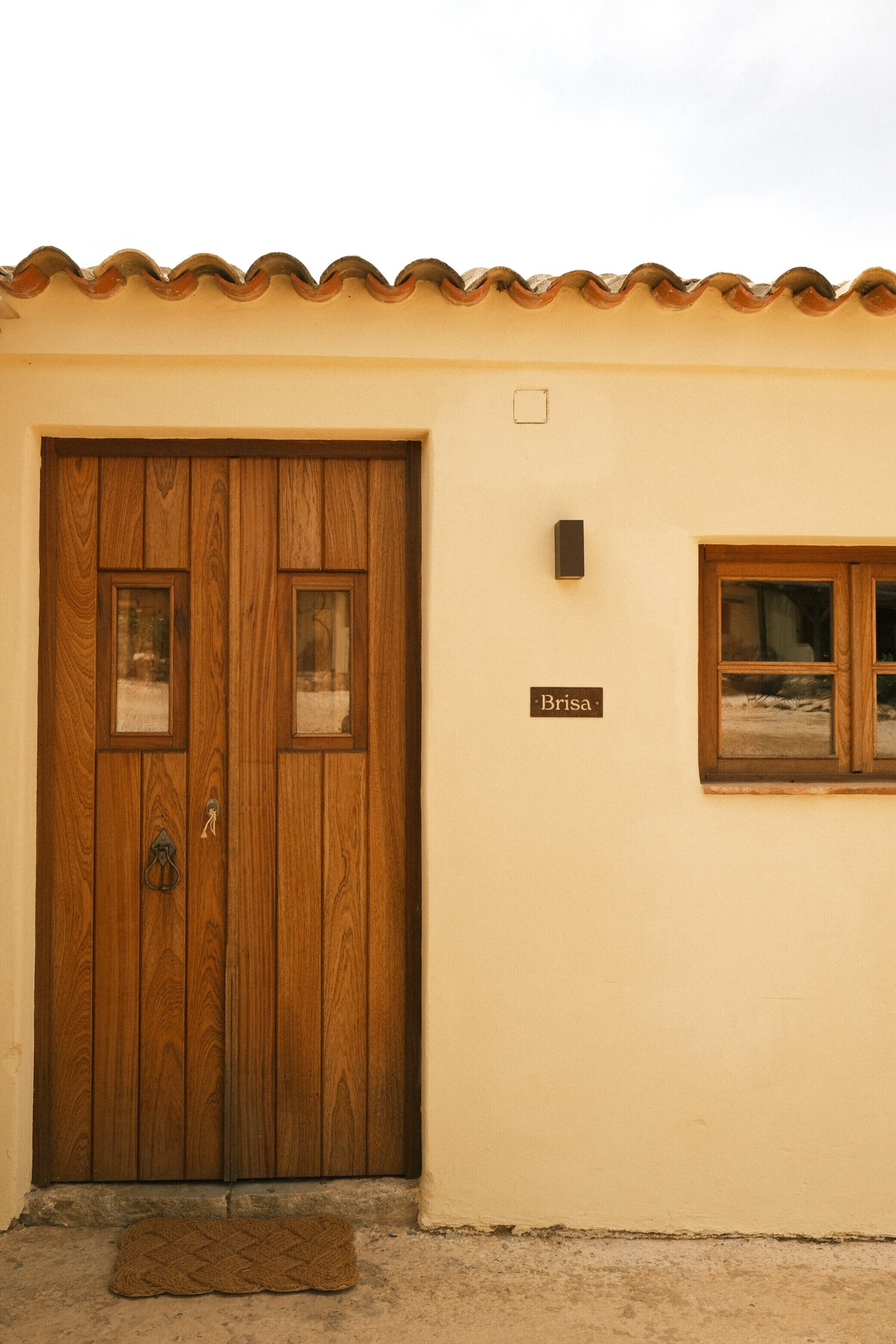 A wooden door with a nameplate, a small window, and a doormat.