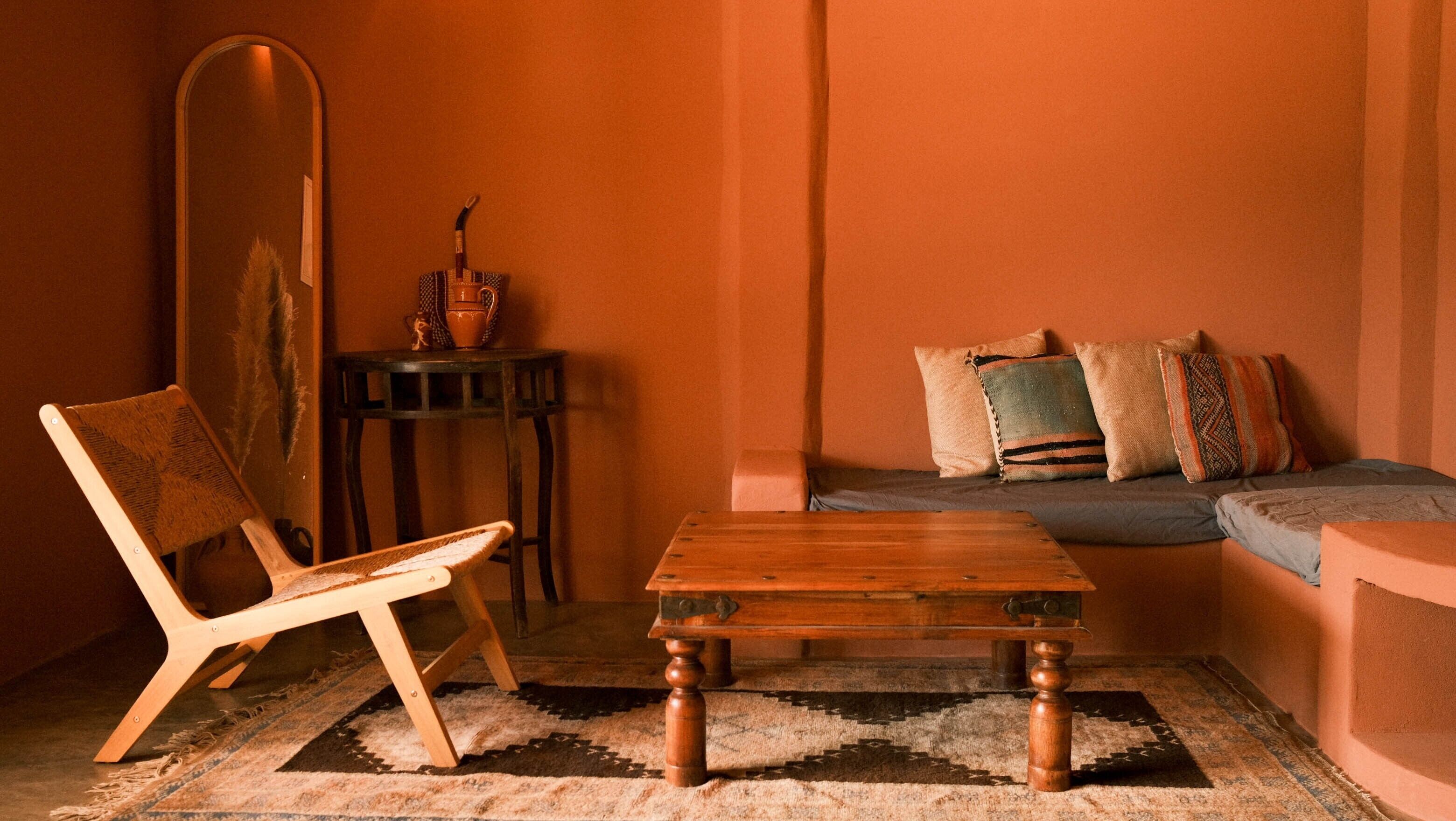 A room with a wooden chair, a small table, a sofa with patterned cushions, and a large mirror on the wall.