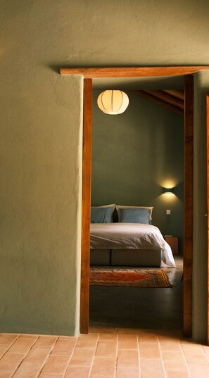 A room with a bed, a wall-mounted light, and a wooden ceiling beam.