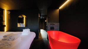 A modern hotel room with a large bed, a red bathtub, and a mirror with a reflection of a person. - Supper boutique suites (Amsterdam)
