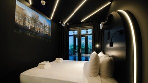 A modern hotel room with a large bed, a cityscape mural, and a view of the outdoors. - Supper boutique suites (Amsterdam)