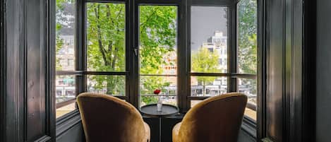 A corner with two chairs facing a window with a view of trees and buildings.