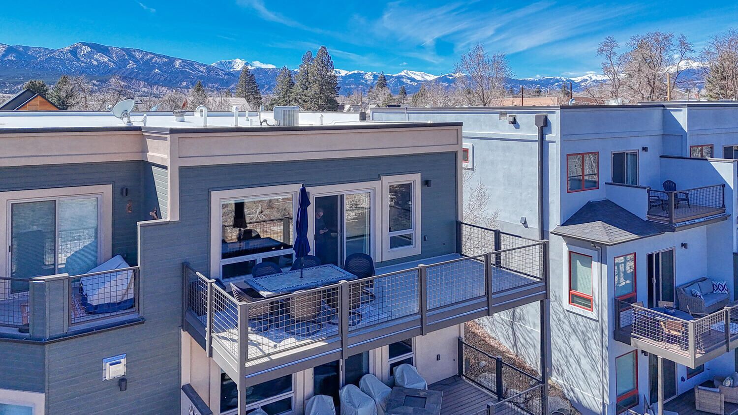 Un edificio residencial moderno de varios pisos con balcones, ventanas amplias y vistas a montañas nevadas.